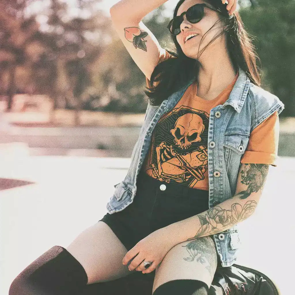 Young woman on her knees, wearing an orange printed t-shirt with a skeleton in a coffin hugging a skateboard